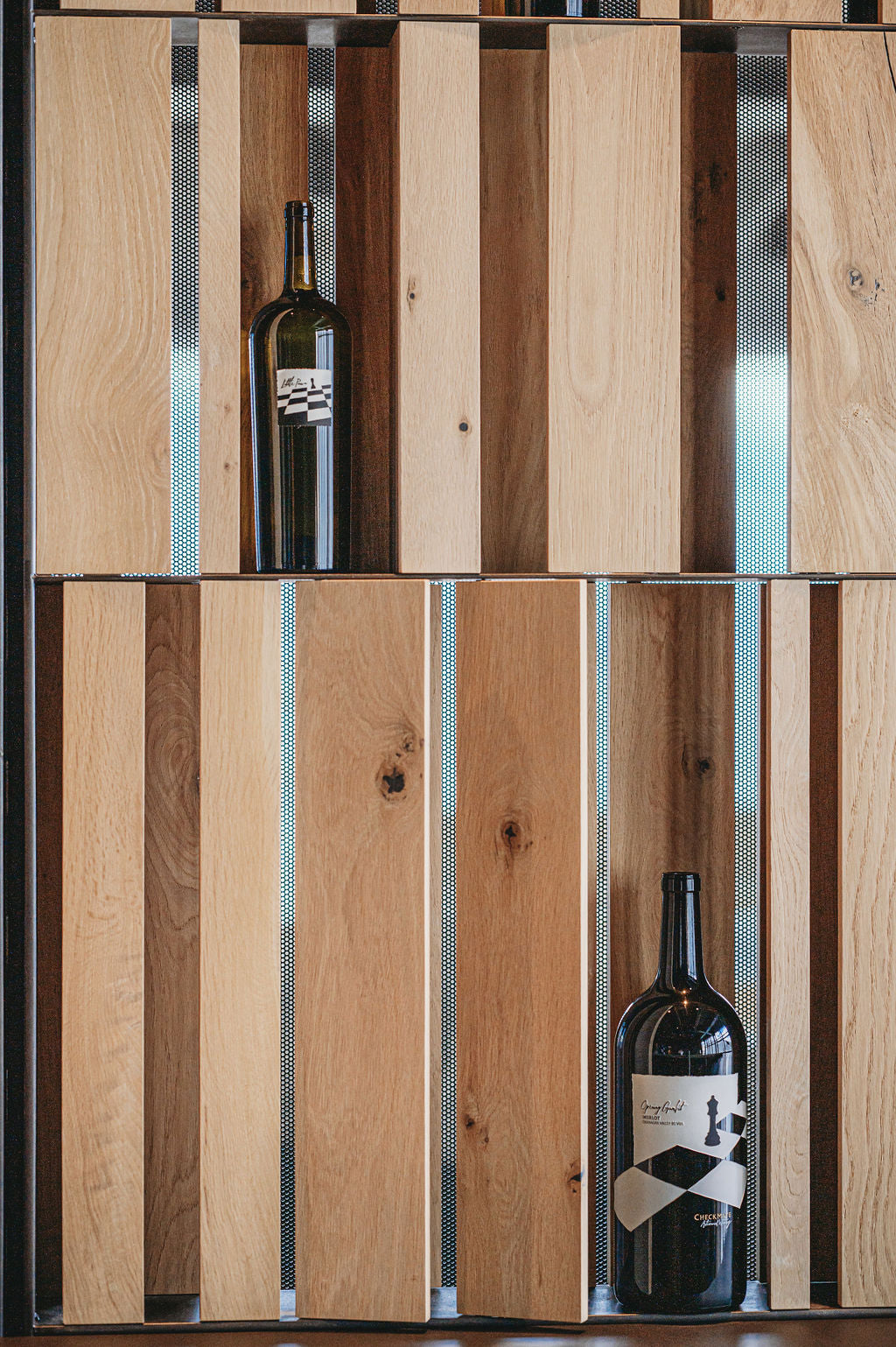 Wine bottles displayed against a wooden panel background. BWP Spaces bespoke furniture and millwork at Checkmate Winery, BC
