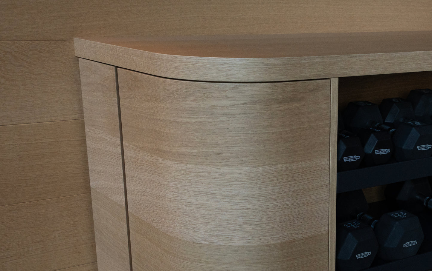 Wooden storage unit with a curved top and shelves containing black dumbbells. BWP Spaces custom millwork in Kelowna, BC