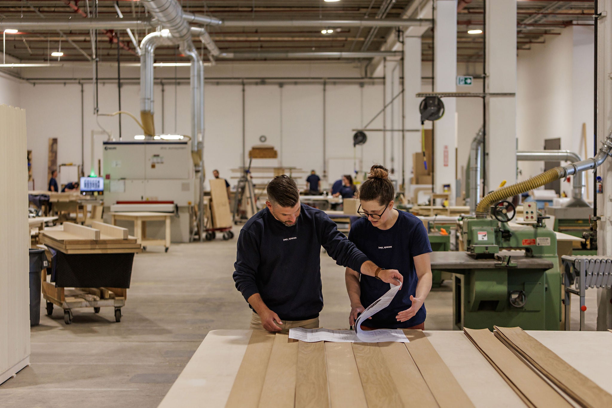 Two people working together in a warehouse setting with wooden panels and machinery. BWP Spaces custom millwork in Kelowna, BC