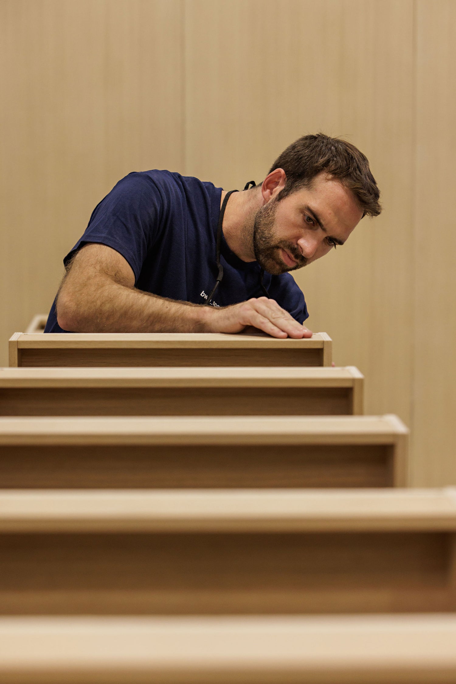 Man in a blue shirt working on wooden stairs against a beige wall. BWP Spaces custom millwork in Kelowna, BC