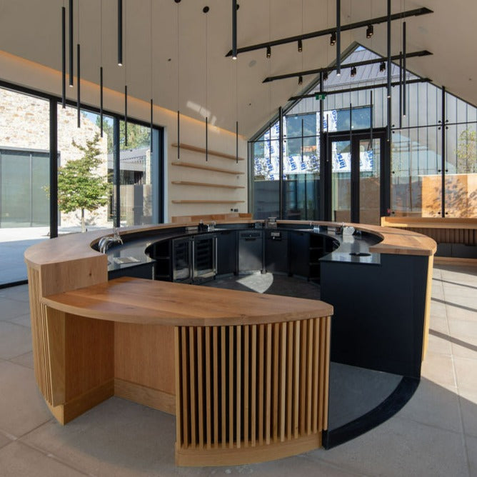 CedarCreek Estate Winery tasting room with custom oval bar featuring solid oak countertop, slatted base, and retail wine display shelving, all crafted by BWP Spaces in collaboration with Erin Martin Design and Arcanum Architecture to create a functional and inviting wine tasting experience