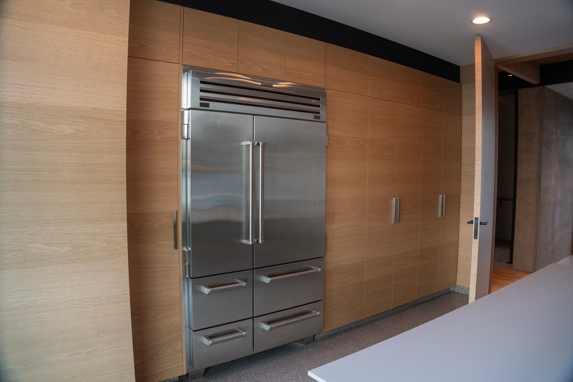 Stainless steel refrigerator in a modern kitchen with wooden walls. BWP Spaces custom millwork in Kelowna, BC