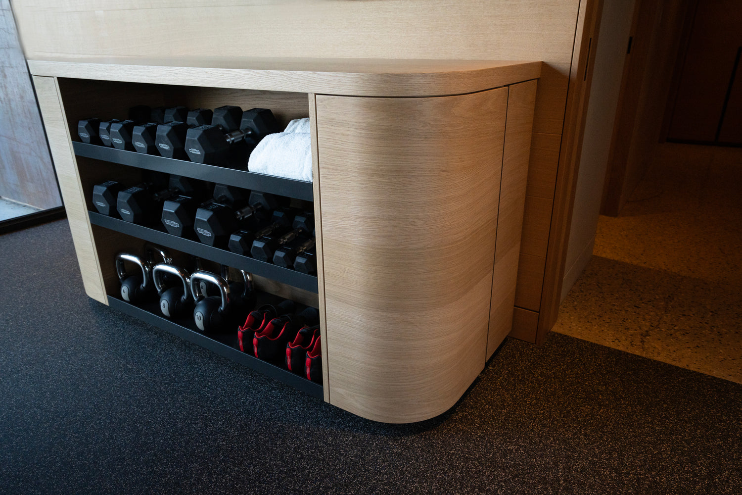Wooden storage unit with shelves holding dumbbells and shoes in a room. BWP Spaces custom millwork in Kelowna, BC